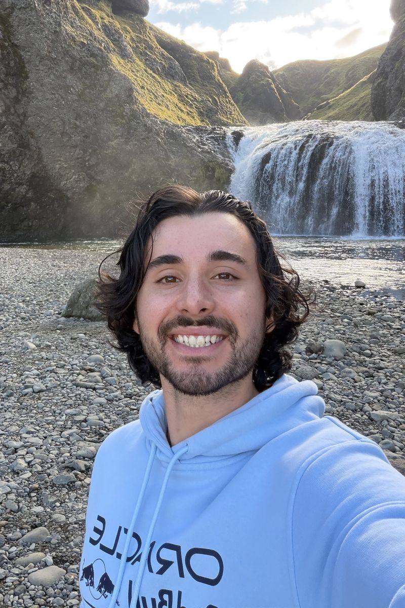 Isaac Darmanin smiling in front of a waterfall